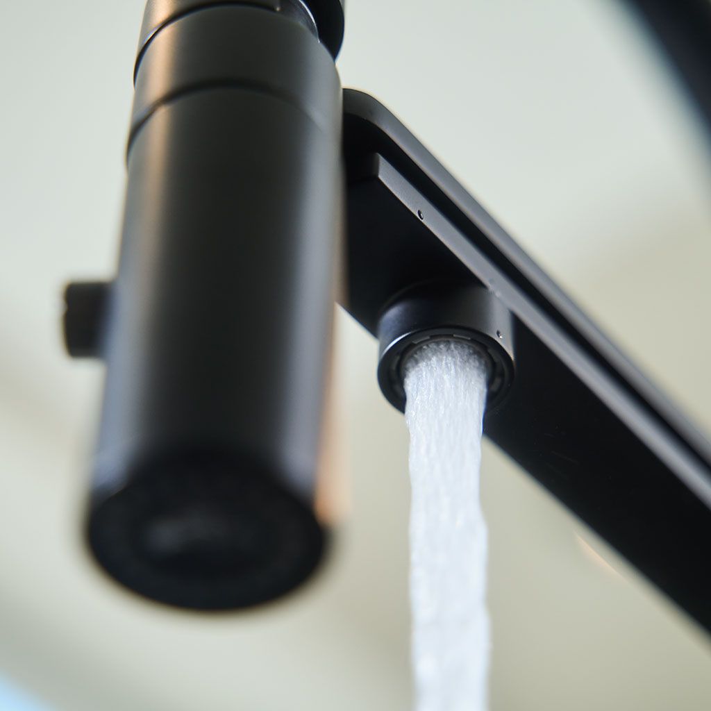 Nahaufnahme der Küchenarmatur Levanto Neo Black 3-Wege-Wasserhahn mit aus dem Auslauf fließendem Wasser, fotografiert aus einem niedrigen Winkel vor einem unscharfen Hintergrund.