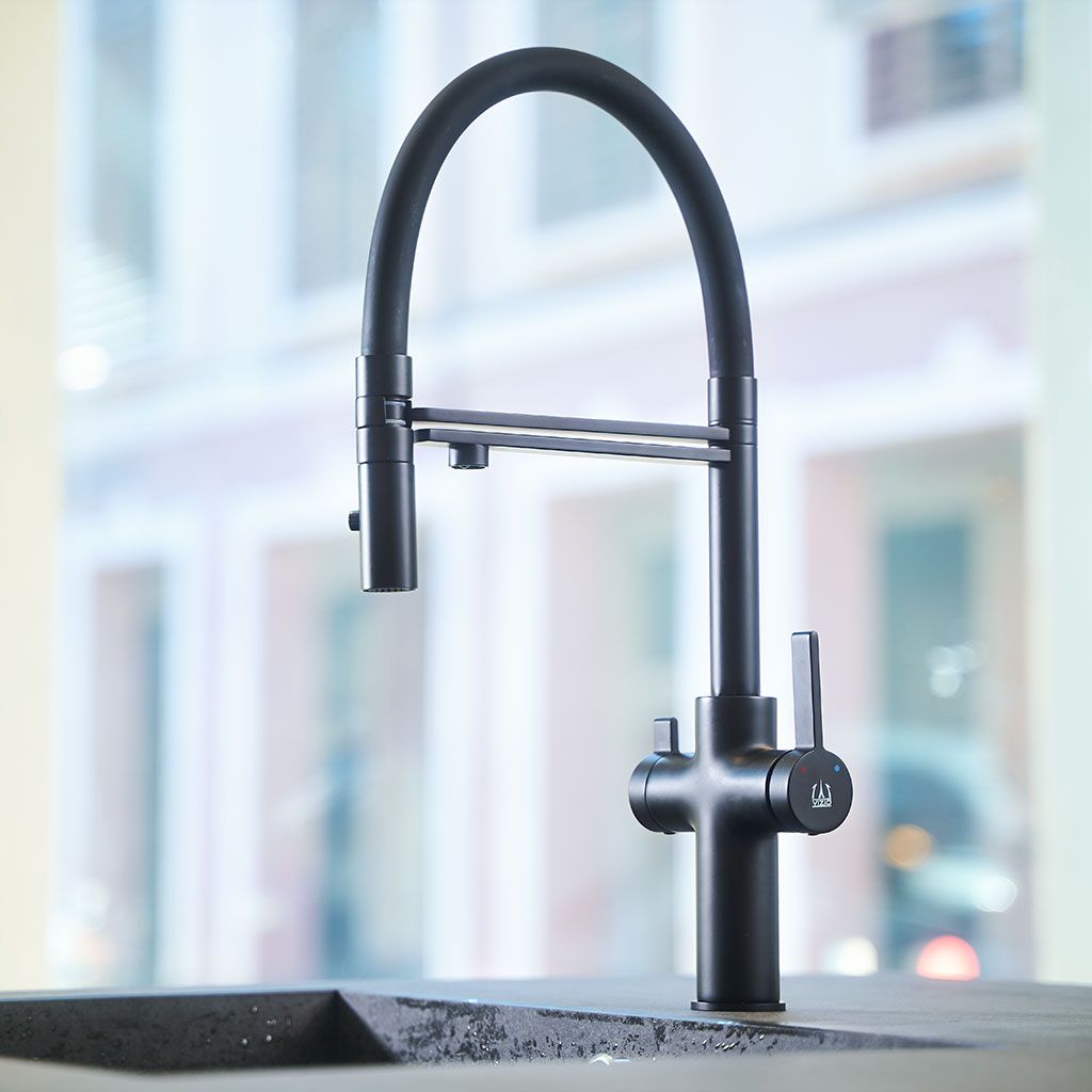 Die Levanto Neo Black 3-Wege-Wasserhahn mit ihrer modernen, mattschwarzen Oberfläche, dem hohen, gebogenen Auslauf und dem seitlichen Griff ist auf einer dunklen Arbeitsplatte mit verschwommenen Fenstern und Gebäuden im Hintergrund installiert.