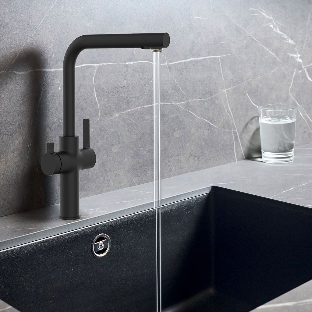 Der Paola NEO Black 3-Wege Wasserhahn gießt Wasser in ein mattschwarzes Waschbecken, das vor einer grauen Marmoraufkantung steht, mit einem Glas Wasser auf der Arbeitsplatte daneben.