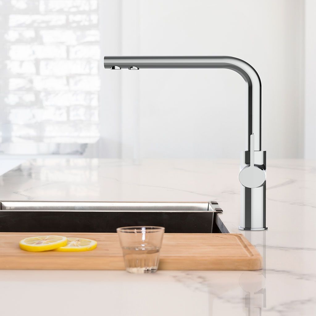 Die Paola NEO 3-Wege-Wasserhahn Chrom steht über einer weißen Marmorarbeitsplatte, daneben ein Holzbrett mit Zitronenscheiben und ein Glas Wasser. Durch das Fenster hinter der Spüle strömt Sonnenlicht herein.