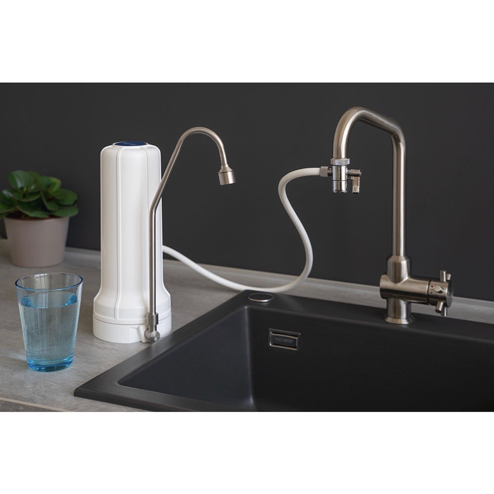 Eine moderne Küchenspüle mit dem Alvito Wasserhahnfilter Pro von Alvito, angeschlossen an einen Schlauch, einem weißen Arbeitsplatten-Wasserfilter und einem Glas Wasser neben einer kleinen Topfpflanze - perfekt für jede Wasserfilter Küche.