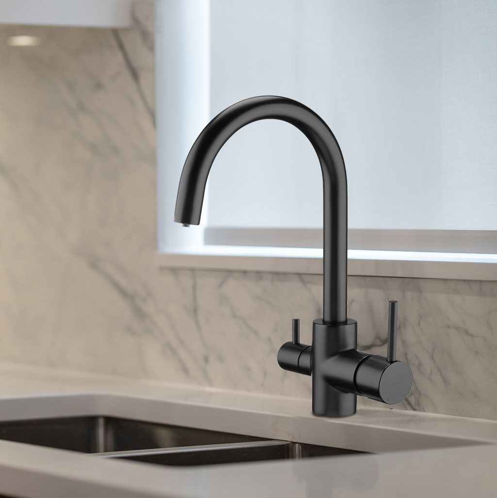 Der Basico Black 3-Wege-Wasserhahn mit zwei Griffen und einem geschwungenen Auslauf ist über einem Waschbecken aus Edelstahl, vor einer Aufkantung aus Marmor und unter einem Fenster mit weißer Blende installiert.