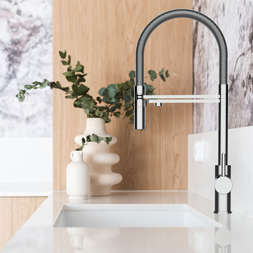 Eine moderne Küchenspüle mit einem hohen, geschwungenen Levanto 3-Wege-Wasserhahn Chrom. Hinter der Spüle befinden sich zwei dekorative Vasen - eine davon mit grünen, blättrigen Zweigen - vor einer Aufkantung in hellem Holz- und Marmorstil.