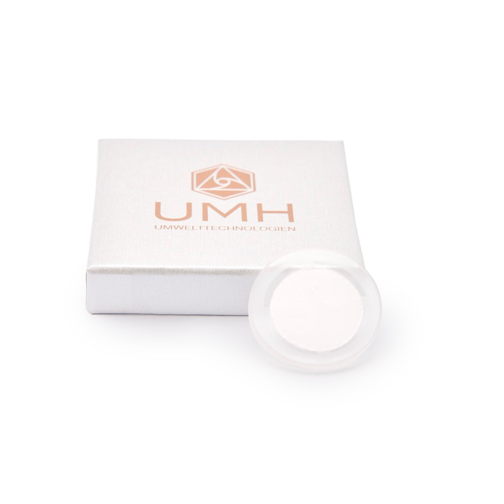 Eine kompakte, runde UMH-Scheibe aus Siliciumoxid liegt vor einer weißen, quadratischen Box mit der Aufschrift UMH UMWELTTECHNOLOGIEN und einem goldenen, geometrischen Logo, das den innovativen Elektrosmog-Schutz auf einem sauberen weißen Hintergrund hervorhebt.