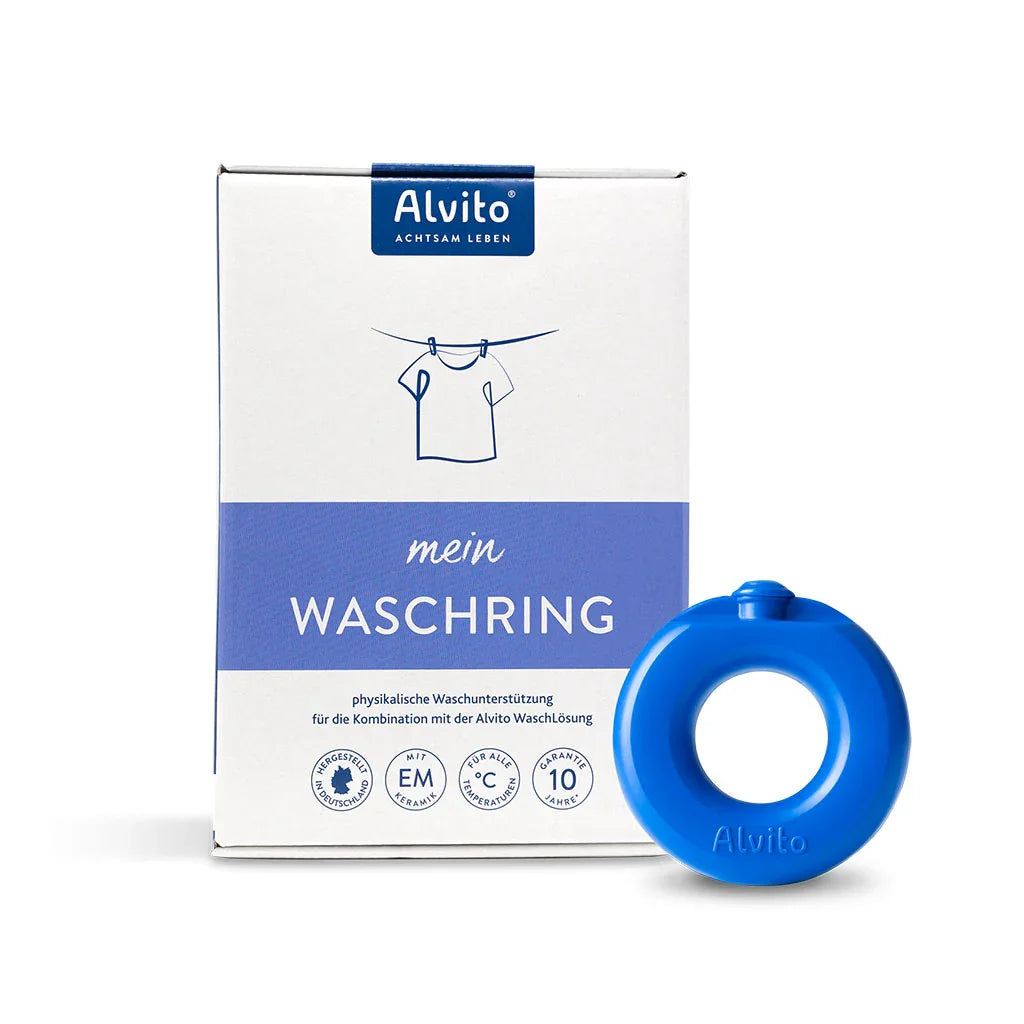 Eine Schachtel mit der Aufschrift Alvito Waschring, die eine einfache Hemdengrafik zeigt, steht neben einem blauen EM-Keramik-Ring. Die Verpackung zeigt Text und Symbole, die den innovativen Ansatz des Alvito Waschrings bei der Wäschepflege betonen.