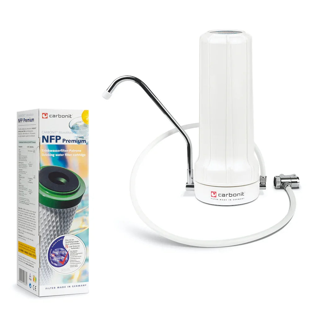 Ein weißer Carbonit SANUNO Auftischfilter mit einem verchromten Wasserhahnadapter ist neben seiner Verpackung abgebildet, auf der Produktdetails und eine Abbildung der NFP Premium Filterpatrone zu sehen sind.