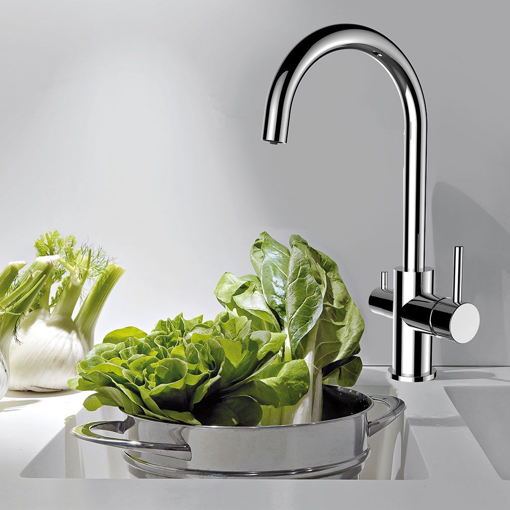 Der Sonstige Furore 3-Wege-Wasserhahn Chrom filtert Wasser über einem Spülbecken, während grünes Blattgemüse in einem Metalltopf gespült wird. Fenchelknollen auf der Arbeitsplatte zeigen die Vorteile von gefiltertem Trinkwasser aus dieser modernen Chrom-Armatur.