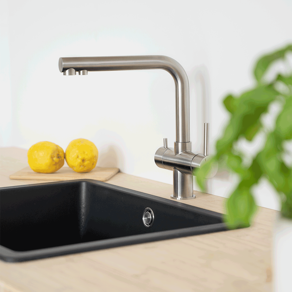 Der Lago 5-Wege-Wasserhahn Edelstahl matt gebürstet - niedrige Variante verleiht Ihrer Küche modernen Stil und ermöglicht täglich frisches, gefiltertes Wasser - hier über einem schwarzen Spülbecken mit Zitronen und grünen Blättern.