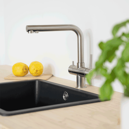 Der Lago 5-Wege-Wasserhahn Edelstahl matt gebürstet - niedrige Variante verleiht Ihrer Küche modernen Stil und ermöglicht täglich frisches, gefiltertes Wasser - hier über einem schwarzen Spülbecken mit Zitronen und grünen Blättern.
