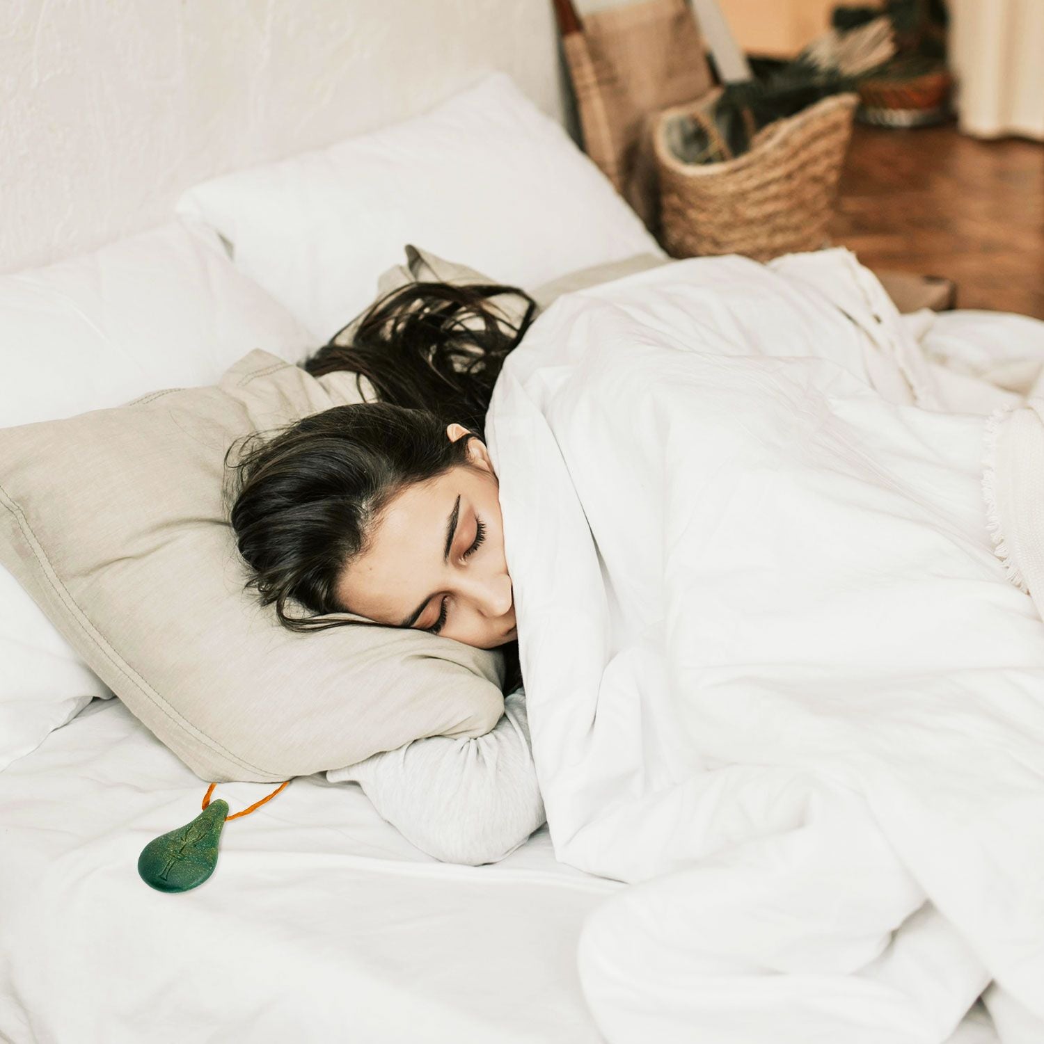 Eine Frau mit langen dunklen Haaren schläft auf der Seite in einem weißen Bett, teilweise zugedeckt mit einer weißen Decke. Ein kleiner grüner Luftqualitätsmonitor liegt auf ihrem Kissen neben ihrem Kopf.