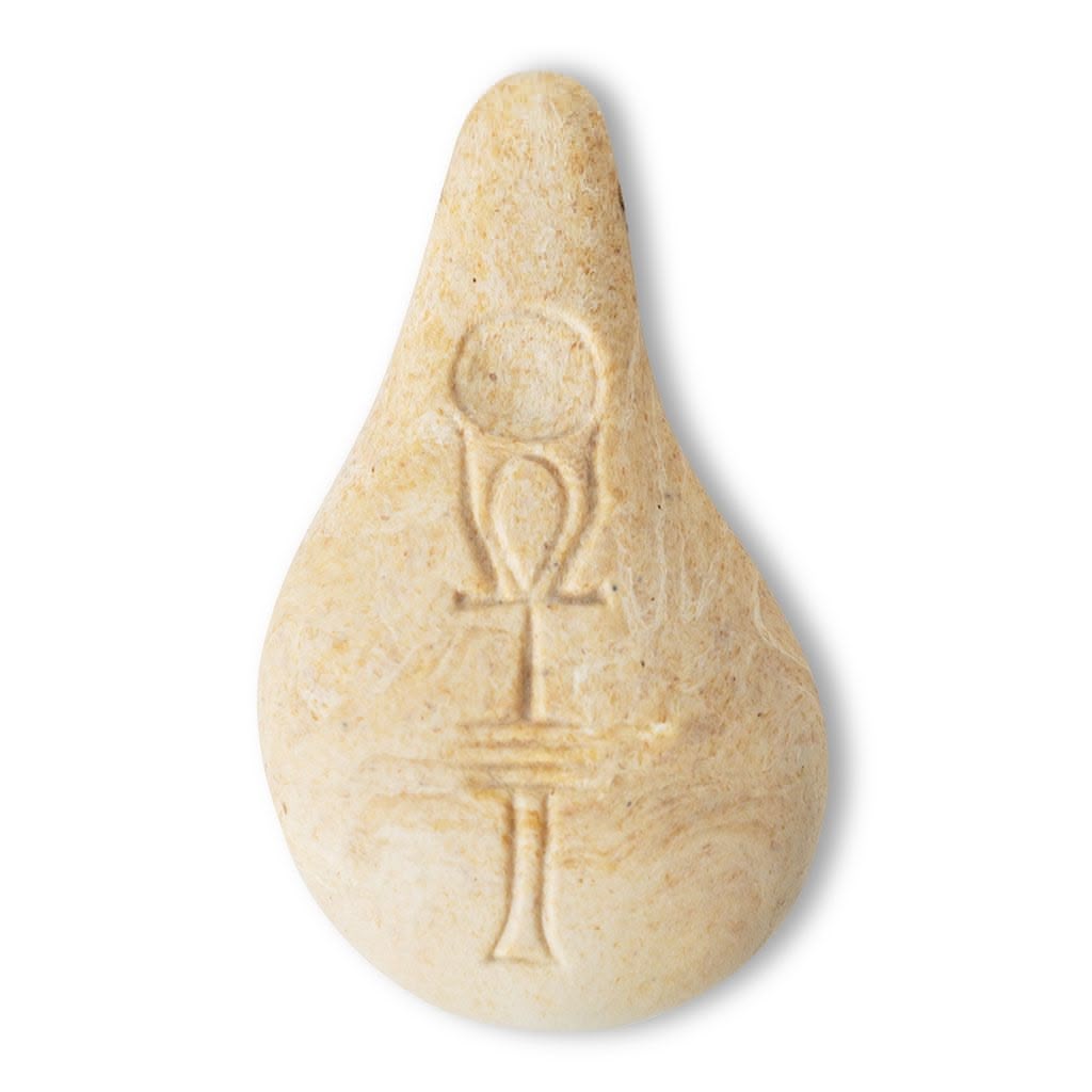 Der Stein der Harmonie ist ein glatter, beigefarbener, tropfenförmiger Stein, in den ein altägyptisches Ankh-Symbol eingraviert ist, das auf einem weißen Hintergrund fotografiert wurde.