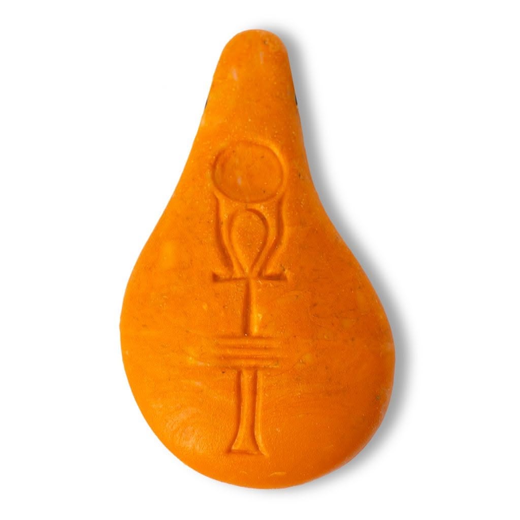 Der Stein der Harmonie ist ein orangefarbener, tropfenförmiger Gegenstand aus organischem Holzgemisch, auf dessen Oberfläche ein Ankh-Symbol eingraviert ist und der sich vor einem weißen Hintergrund befindet.