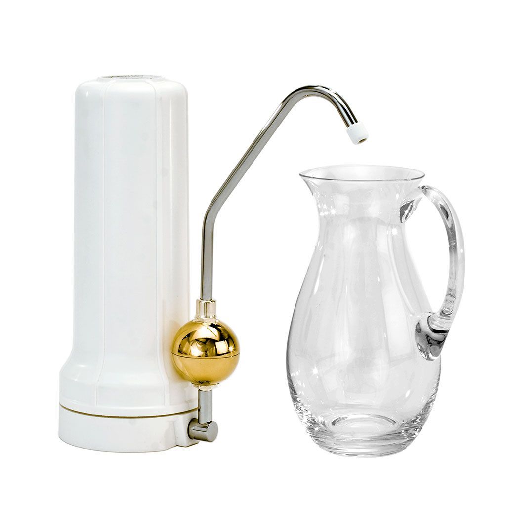 Eine UMH Live - Wasserbelebung direkt am Wasserhahn (Gold &amp; Rhodium) ist neben einem klaren Glaskrug auf weißem Hintergrund abgebildet - perfekt, um Ihr Trinkwassererlebnis aufzuwerten.