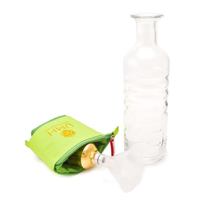 Eine klare Glasflasche steht aufrecht neben einem grünen Beutel mit Reißverschluss, der das UMH Pure Travel enthält, ein goldenes und klares Wasserenergetisierungssystem zur Herstellung von hexagonalem Wasser, das teilweise sichtbar ist, wenn der Beutel geöffnet ist.