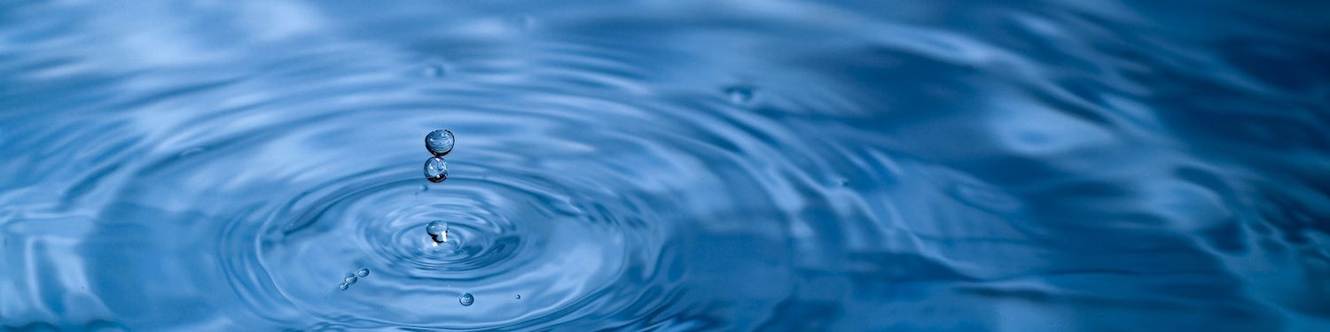 Eine Nahaufnahme von Wassertropfen, die in ein ruhiges blaues Becken fallen und kreisförmige Wellen erzeugen, die sich auf der Wasseroberfläche ausbreiten.